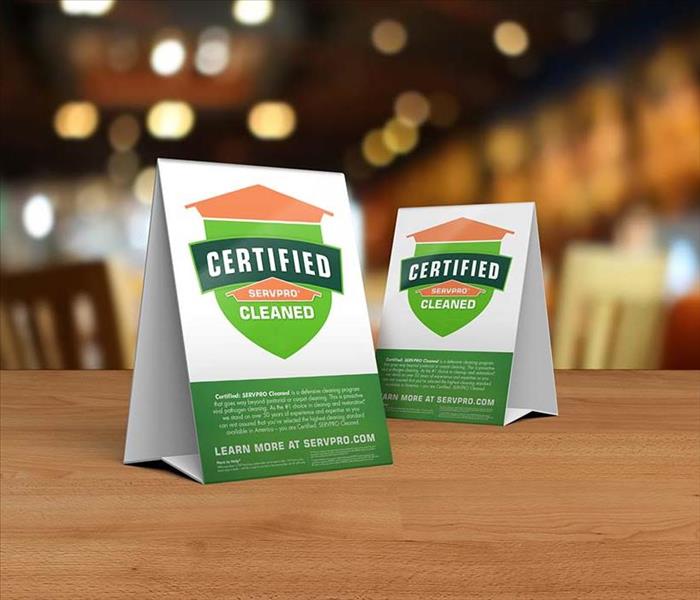 Table tent signs describing the Certified: SERVPRO Cleaned program on top of a wooden table